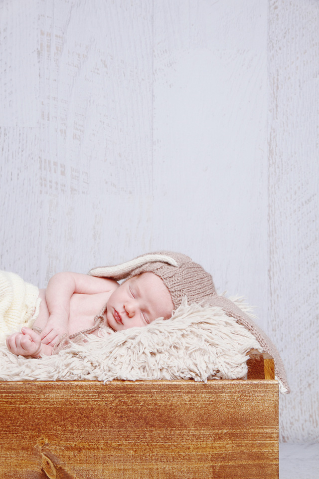 Photo of a newborn with bunny ears as an accessory, lying in a wooden box.