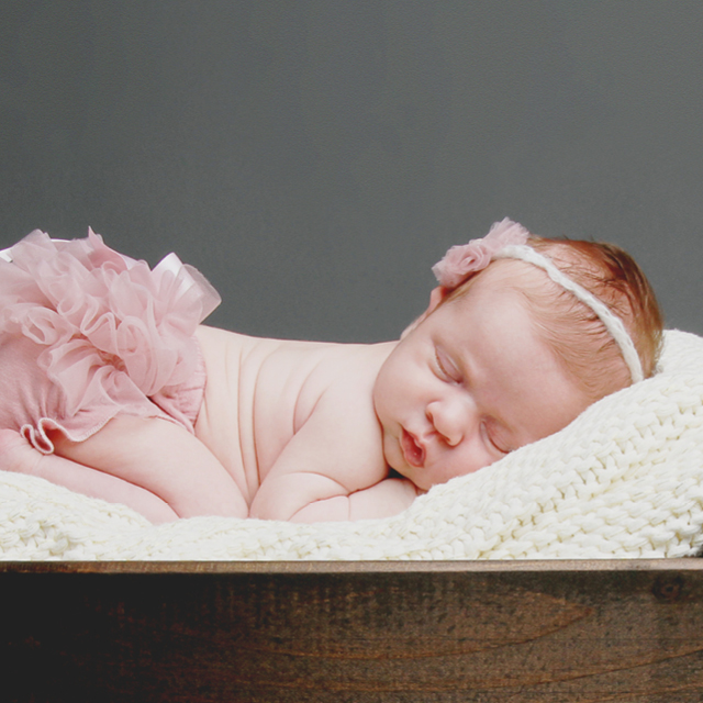 Photo of a newborn wearing a pink tutu and sleeping in a wooden box.