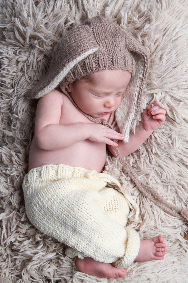 Photo of a newborn wearing bunny ears as an accessory, lying on a cozy blanket.