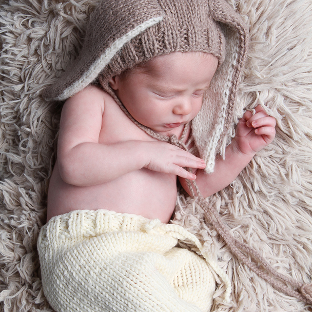 Photo of a newborn wearing bunny ears as an accessory, lying on a cozy blanket.