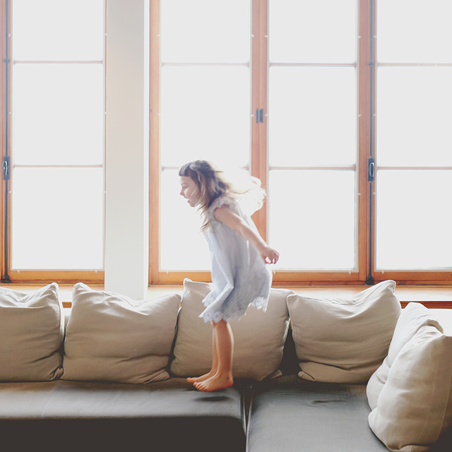 Photo of a little girl at home jumping on a couch.