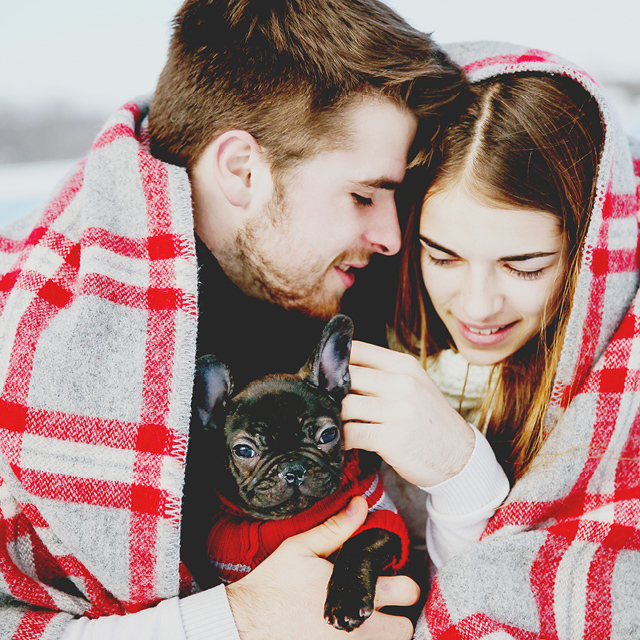Photo in exterior of a young couple hugging themselves in wool blankets.