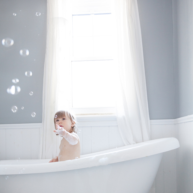Photo of a child in a bath and looking at the soap bubbles.