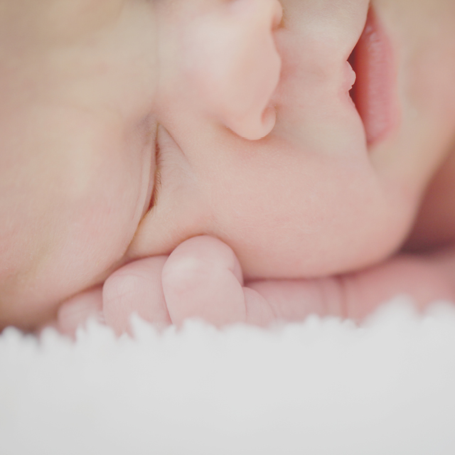 Photo of a close-up of a newborn sleeping on a cozy blanket at home.