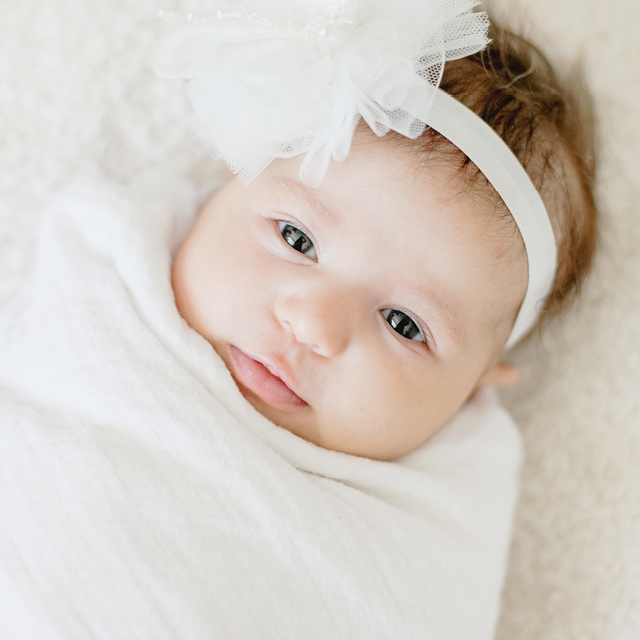 Photo of a newborn baby wrapped in a white blanket and wearing a fabric flowers headband.