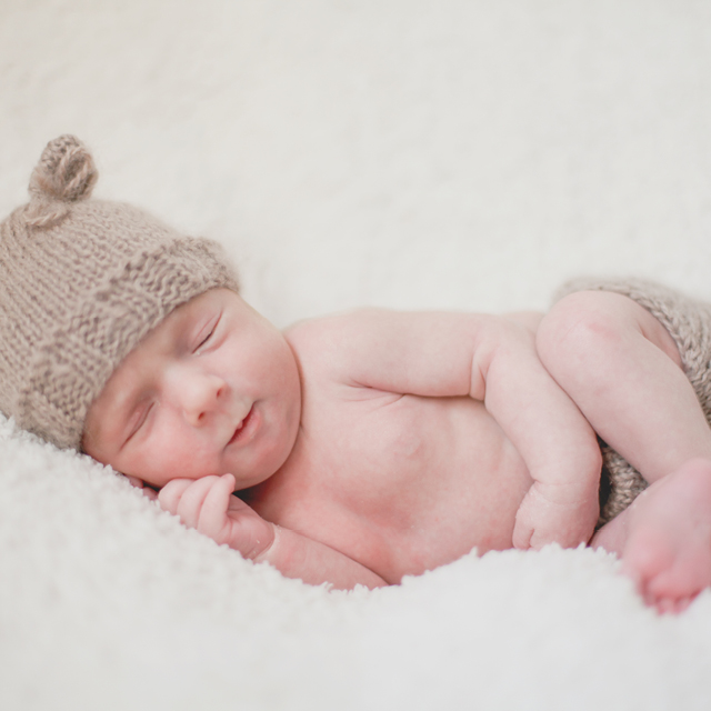 Photo of a newborn lying on a cozy blanket and wearing a bear ears beanie as a photo accessory.