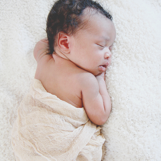 Photo of a newborn sleeping peacefully on a white blanket.