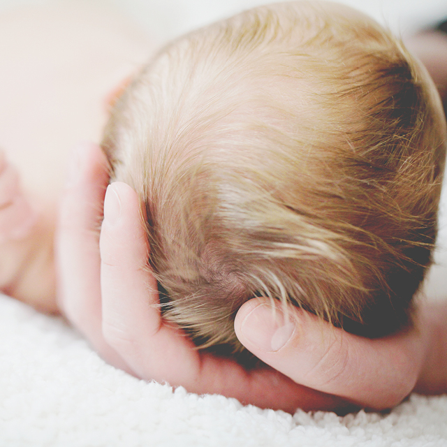 Photo of a mother gently lifting a newborn's head.