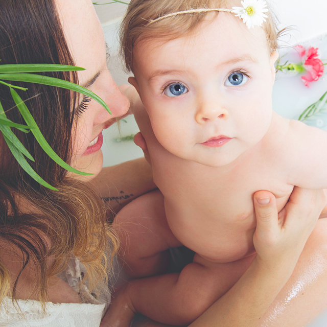 Photo of a mother and her baby in a milky bath decorated with fresh flowers.