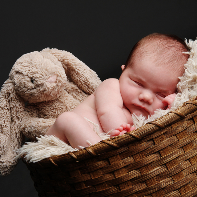 Une photo d'un nouveau-né couché dans un panier en osier accompagné d'un lapin en peluche.