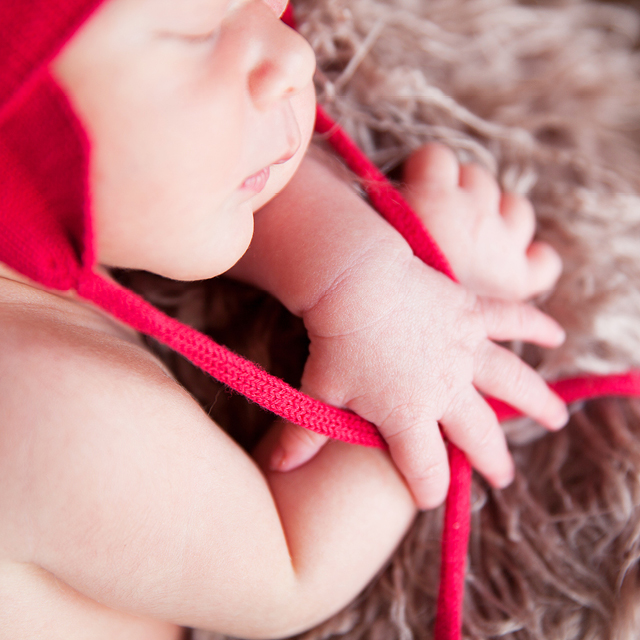 Photo à la maison d'un nouveau-né endormi et portant une tuque rouge.