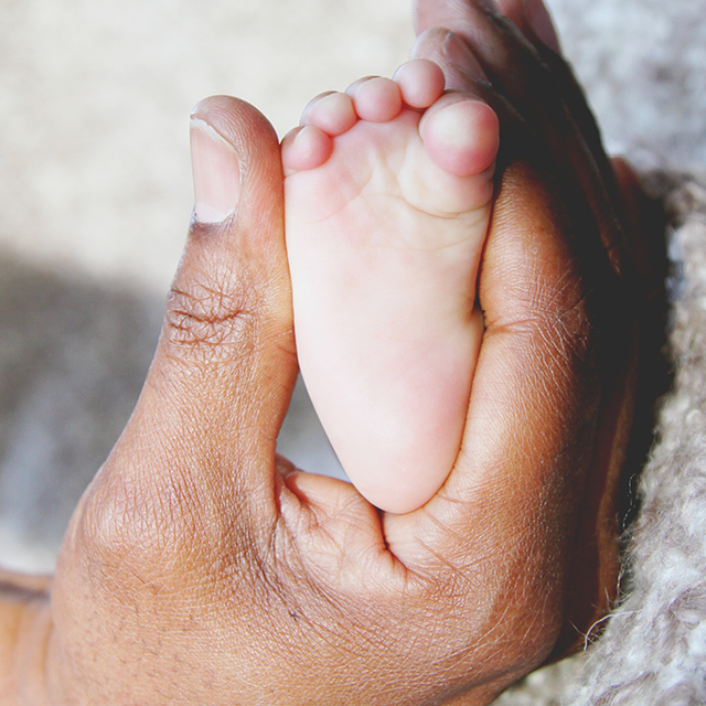 Photo à la maison de la main d'un papa caressant le petit pied de son nouveau-né.