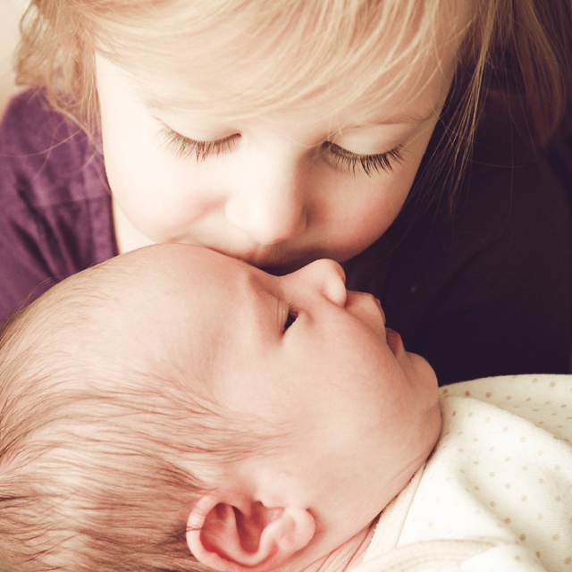 Photo à la maison d'une petite fille donnant un bisou à un nouveau-né.