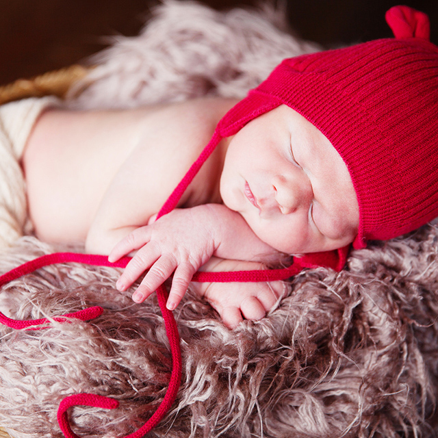Photo d'un nouveau-né endormi et portant une tuque rouge en laine avec de petites oreilles.