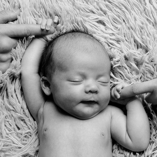 photographie d'un bébé endormi tenant la main de ses parents